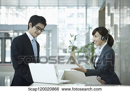 Stock Photograph - a help desk woman explaining to businessman through laptop. Fotosearch