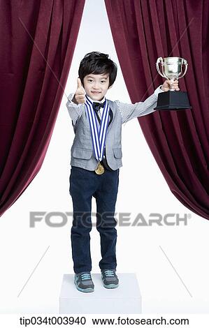 a kid posing with a trophy cup in front of a red curtains View Large Photo Image Stock Image - a kid posing with a trophy cup in front of a red curtains. Fotosearch
