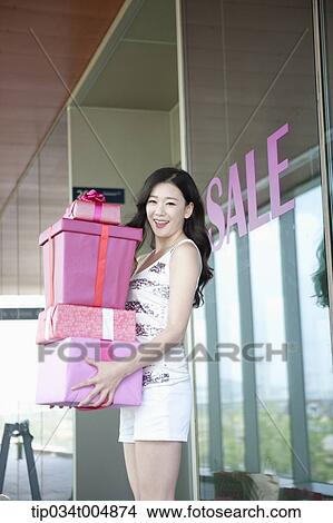 Picture - a lady holding piles of presents in front of a show window with a sale sign. Fotosearch