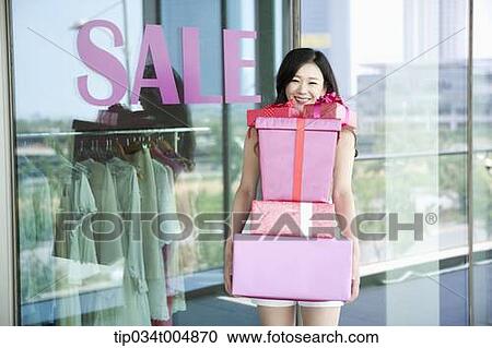 Stock Image - a lady holding piles of presents in front of a show window with a sale sign. Fotosearch