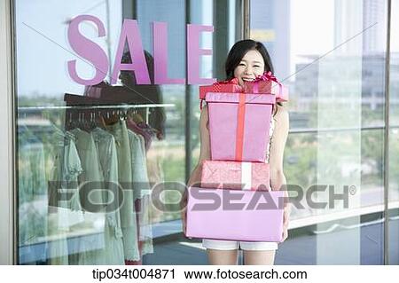 a lady holding piles of presents in front of a show window with a sale sign View Large Photo Image Stock Image - a lady holding piles of presents in front of a show window with a sale sign. Fotosearch