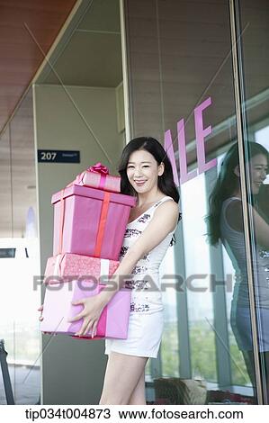 Stock Image - a lady holding piles of presents in front of a show window with a sale sign. Fotosearch