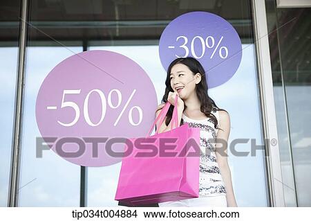 a lady holding shopping bags smiling in front of a show window during sale View Large Photo Image Picture - a lady holding shopping bags smiling in front of a show window during sale . Fotosearch