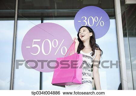 a lady holding shopping bags smiling in front of a show window during sale View Large Photo Image Stock Photograph - a lady holding shopping bags smiling in front of a show window during sale . Fotosearch
