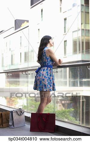 a lady in dress looking out in a building balcony with shopping bags on the floor View Large Photo Image Stock Image - a lady in dress looking out in a building balcony with shopping bags on the floor. Fotosearch