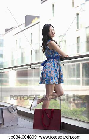 Stock Photo - a lady in dress posing in a building balcony with shopping bags on the floor. Fotosearch