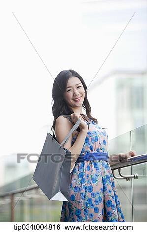 a lady in flower printed dress posing while holding shopping bag View Large Photo Image Stock Photograph - a lady in flower printed dress posing while holding shopping bag. Fotosearch