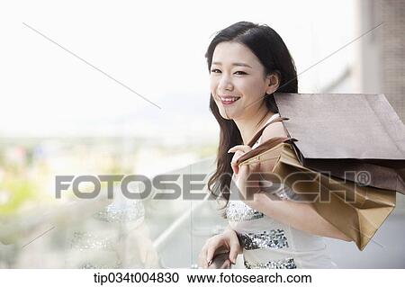 Stock Image - a lady in silver-white striped sleeveless shirt smiling with shopping bags in her hand. Fotosearch