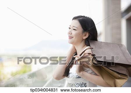 Stock Image - a lady in silver-white striped sleeveless shirt smiling with shopping bags in her hand. Fotosearch