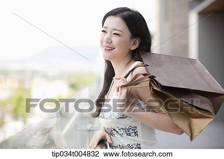 Stock Image - a lady in silver-white striped sleeveless shirt smiling with shopping bags in her hand. Fotosearch