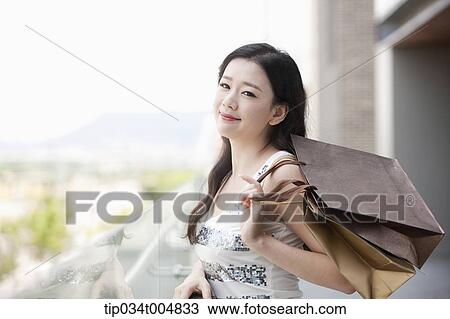 Stock Image - a lady in silver-white striped sleeveless shirt posing with shopping bags . Fotosearch