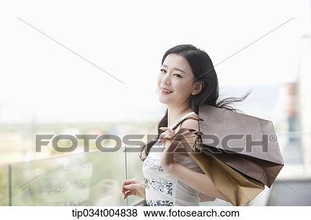 Stock Photo - a lady in silver-white striped sleeveless shirt posing with shopping bags . Fotosearch