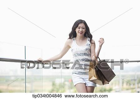 Stock Photograph - a lady in silver-white striped sleeveless shirt posing with shopping bags . Fotosearch