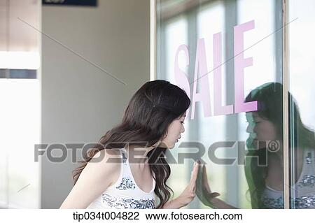 Stock Image - a lady looking on a show window with a sale sign. Fotosearch