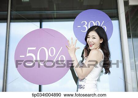 Stock Image - a lady smiling in front of a show window with sale signs. Fotosearch