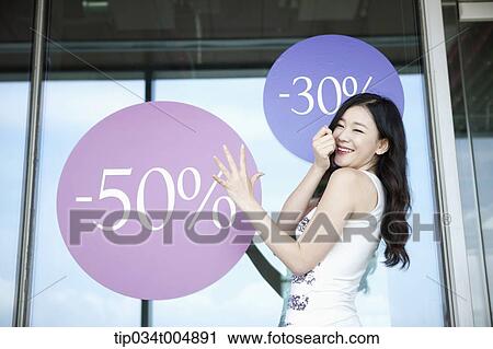 Stock Image - a lady smiling in front of a show window with sale signs. Fotosearch