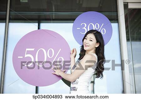 Stock Image - a lady smiling in front of a show window with sale signs. Fotosearch