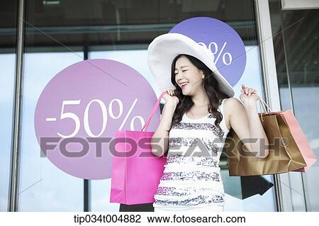 a lady wearing hat holding shopping bags smiling in front of a show window during sale View Large Photo Image Stock Image - a lady wearing hat holding shopping bags smiling in front of a show window during sale . Fotosearch
