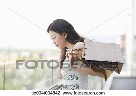 Stock Image - a lady with shopping bags looking down at building balcony. Fotosearch