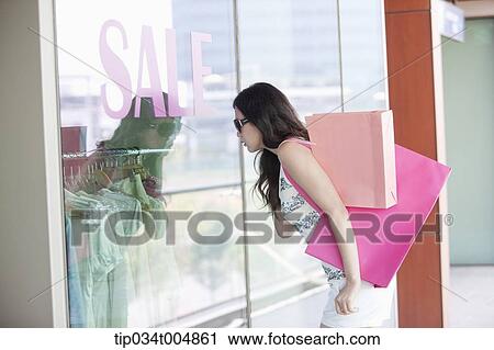 Stock Image - a lady with sunglasses and shopping bags window shopping during sale. Fotosearch