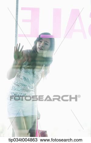 Stock Image - a lady with sunglasses and shopping bags window shopping during sale. Fotosearch