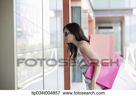 Stock Photo - a lady with sunglasses and shopping bags looking on a show window. Fotosearch
