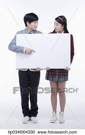 Stock Image - a male and female students with school uniform holding a big empty white paper . Fotosearch