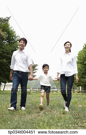 Stock Image - a male kid and parents walking hand in hand on grass . Fotosearch
