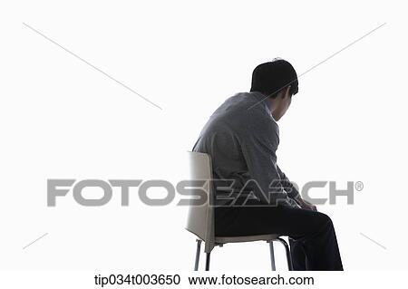 Stock Image - a male student sitting on a chair under a dark shadow. Fotosearch