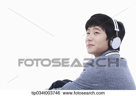Stock Photograph - a male student sitting while wearing a headphone. Fotosearch