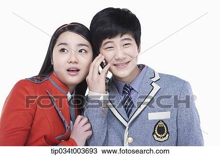 Stock Image - a male student talking on a mobile phone while female student tries to overhear. Fotosearch