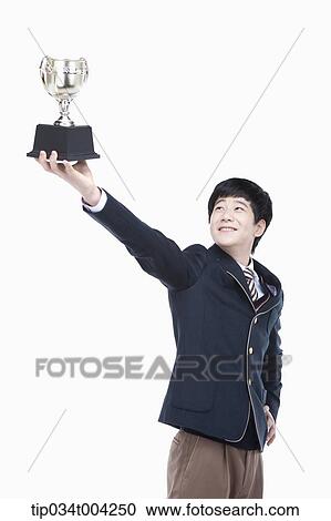 Stock Image - a male student wearing school uniform holding up a trophy cup. Fotosearch