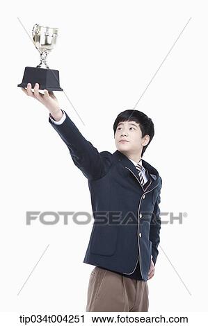 Stock Image - a male student wearing school uniform holding up a trophy cup. Fotosearch