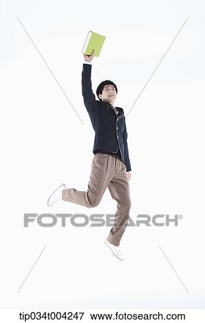 Stock Photo - a male student wearing school uniform jumping while holding a book. Fotosearch