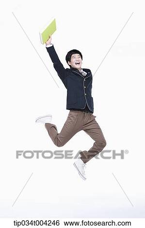 Stock Photograph - a male student wearing school uniform jumping while holding a book. Fotosearch