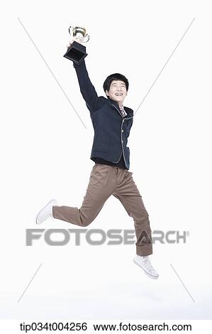 Stock Photograph - a male student wearing school uniform jumping with a trophy cup. Fotosearch
