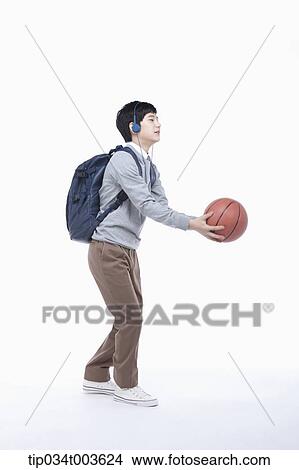 Picture - a male student with headphones catching a basketball. Fotosearch