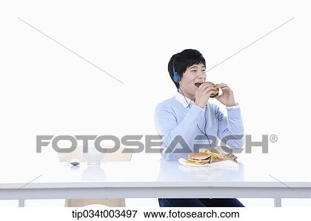 Stock Photo - a male student with headphones having a burger . Fotosearch
