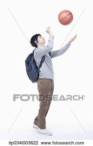 Stock Image - a male student with headphones shooting a basketball in the air. Fotosearch