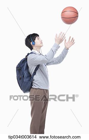 Picture - a male student with headphones throwing a basketball in the air. Fotosearch