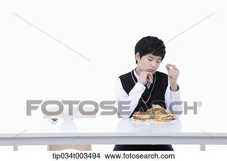 Picture - a male student with school uniform thinking he should have small bites of burgers. Fotosearch