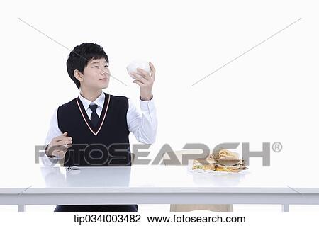 Stock Image - a male student with school uniform holding up a rice bowl. Fotosearch