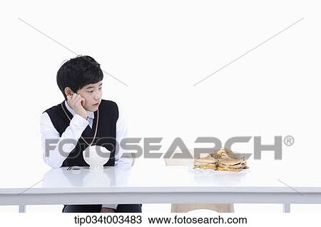 Stock Image - a male student with school uniform staring at burgers while sitting in front of rice bowl. Fotosearch