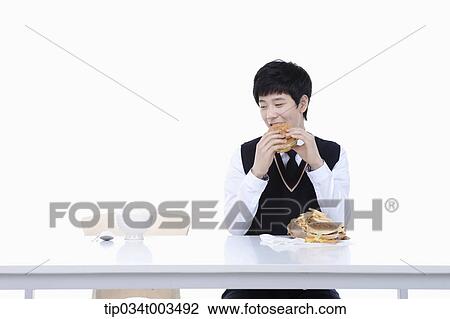 Stock Image - a male student with school uniform eating burgers while staring at rice next to him. Fotosearch