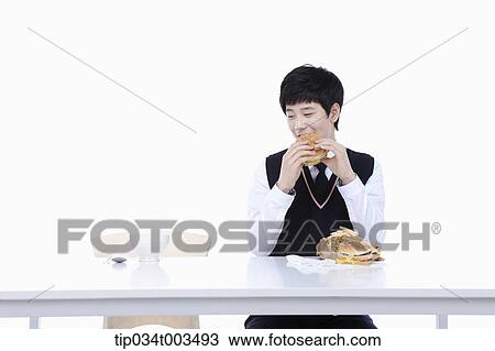 Stock Image - a male student with school uniform eating burgers while staring at rice next to him. Fotosearch