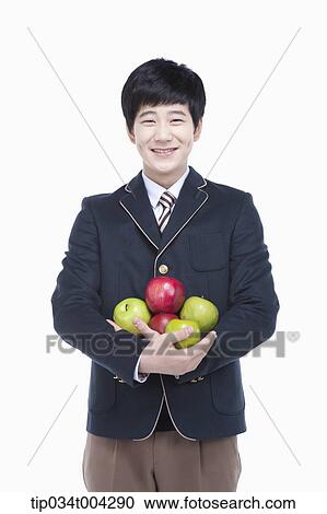 Stock Image - a male student with school uniform holding apples in his arms . Fotosearch