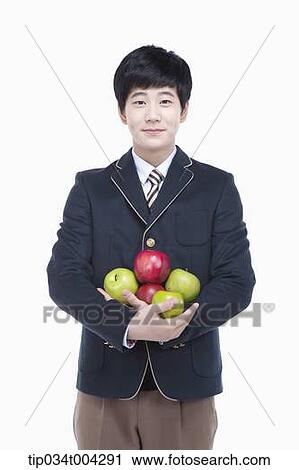 Stock Image - a male student with school uniform holding apples in his arms . Fotosearch