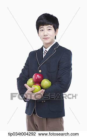 Stock Image - a male student with school uniform holding apples in his arms . Fotosearch
