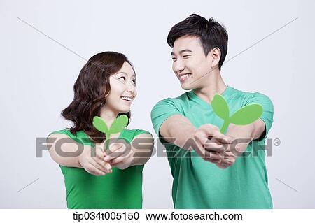 Stock Image - a man and a woman facing each other while holding big sprouts. Fotosearch