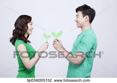 Stock Image - a man and a woman facing each other while holding big sprouts. Fotosearch